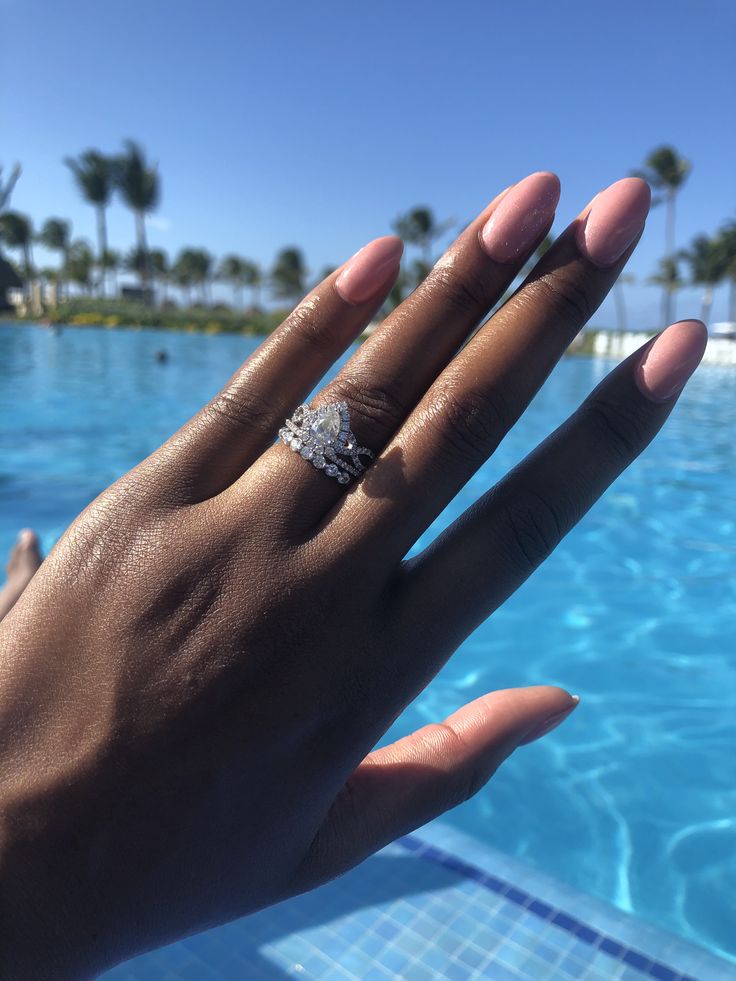 a person's hand with a ring on it near a swimming pool