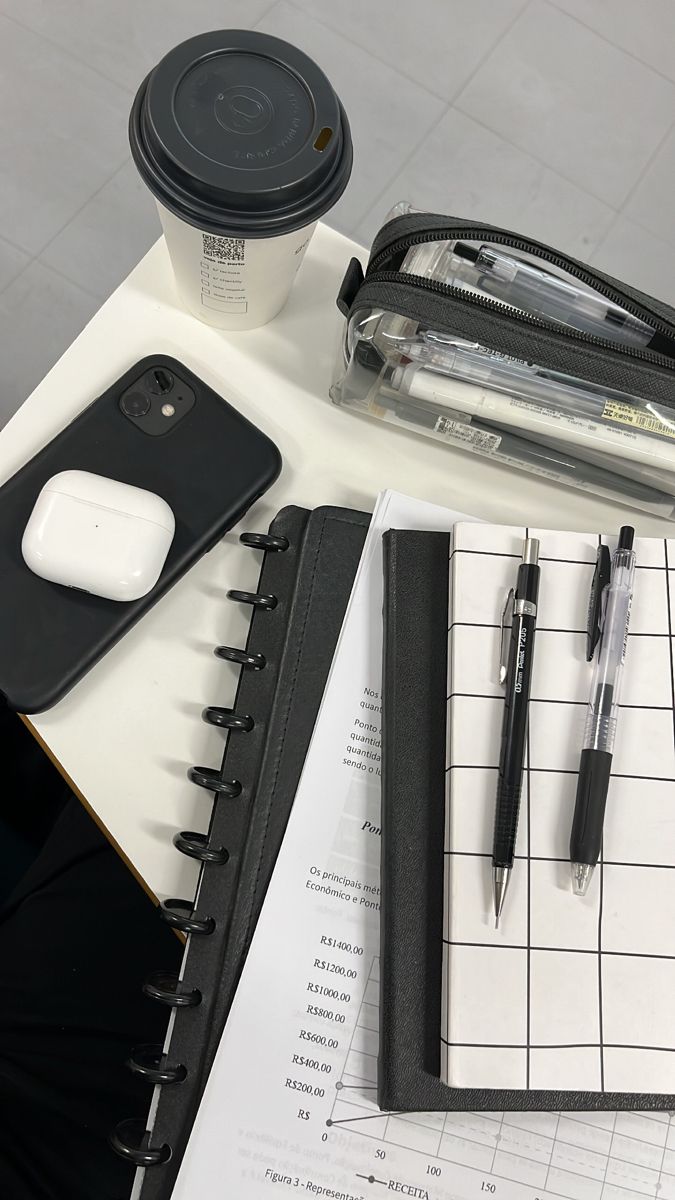 a desk with notebooks, pen and coffee cup on it next to a cell phone