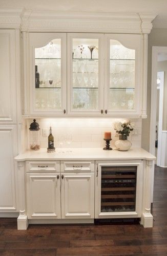 a kitchen with white cabinets and wood flooring is pictured in this image, there are two wine glasses on the cabinet doors