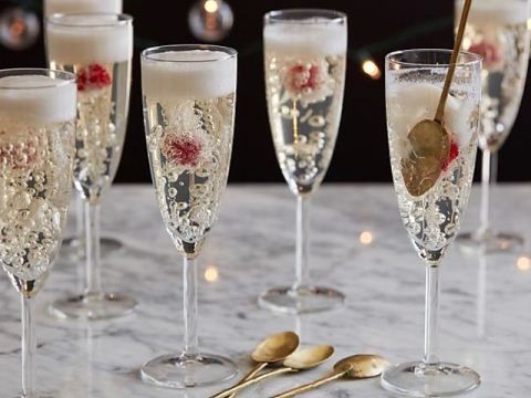 five champagne flutes lined up on a table with gold spoons and candles in the background