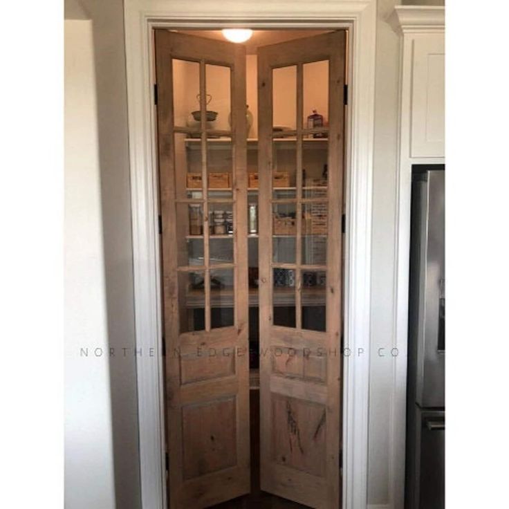 an open wooden door in a kitchen with white walls and wood trimming on the doors