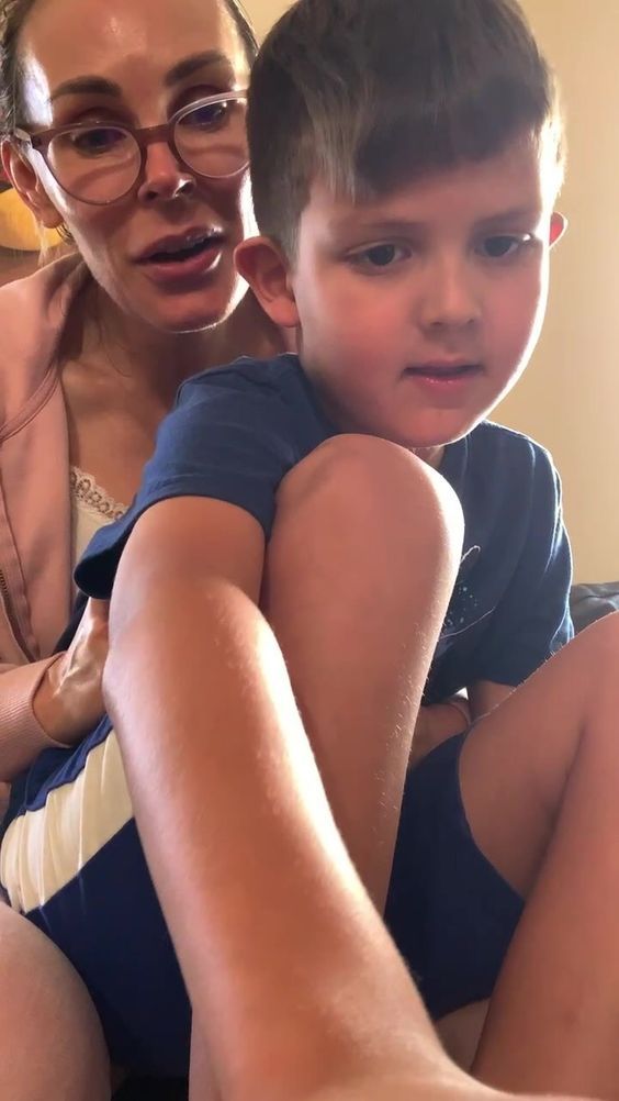 a woman sitting next to a little boy on top of a bed with his legs crossed