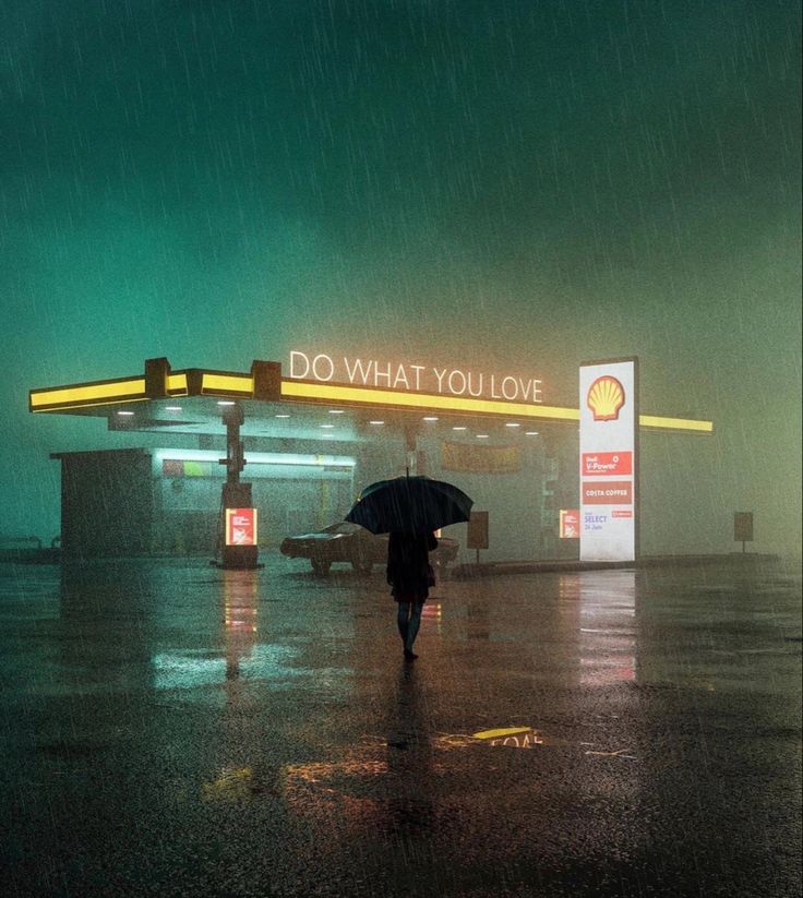 a person walking in the rain with an umbrella near a gas station that says do what you love