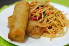 a white plate topped with fried food next to noodles and sauce on a green tablecloth