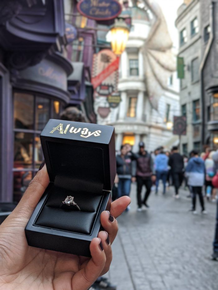 a person holding up an engagement ring in front of a store on a street corner