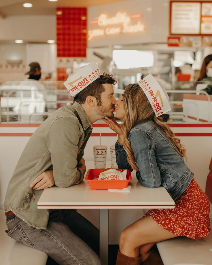 a man and woman sitting at a table in a fast food restaurant kissing each other