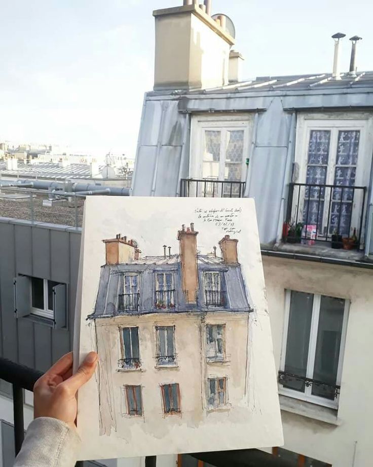 a person holding up a drawing in front of a building with windows and balconies