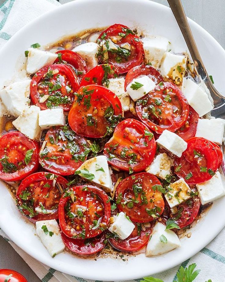 a white plate topped with sliced tomatoes and feta cheese