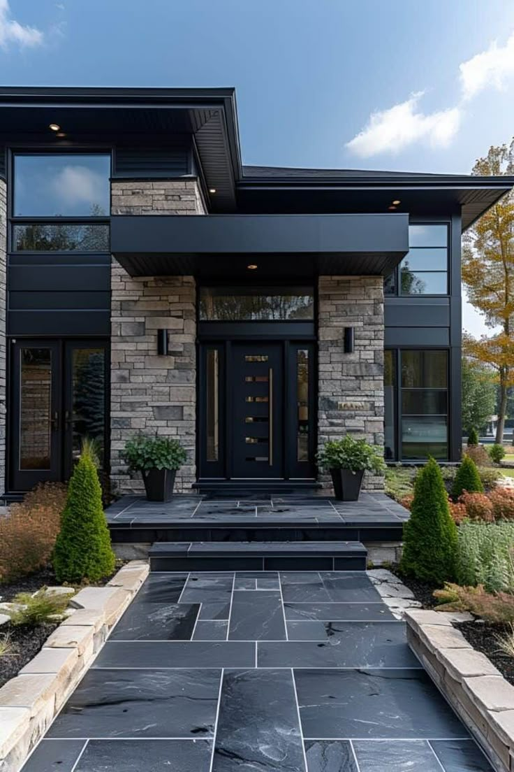 a modern home with stone and black exterior, large front door and steps leading up to the entrance