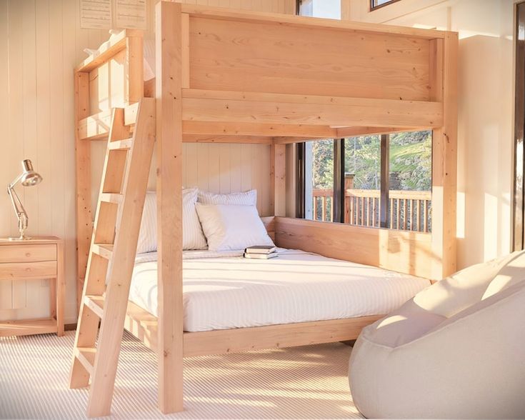 a wooden bunk bed sitting in a bedroom next to a white chair and table with two windows