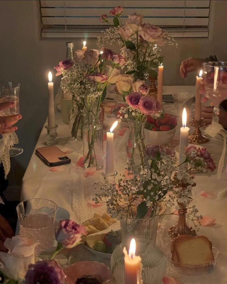 the table is set with candles and flowers in vases, plates and bread on it