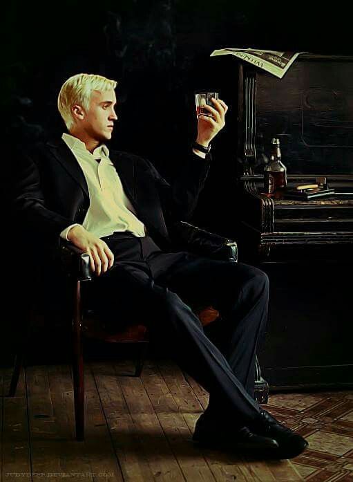 a man in a suit sitting on a chair holding a wine glass and looking at his cell phone