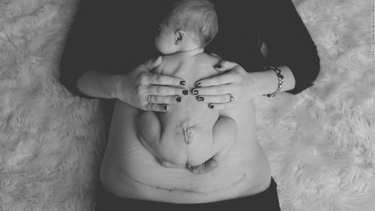 a woman holding a baby in her arms while laying on top of a white blanket