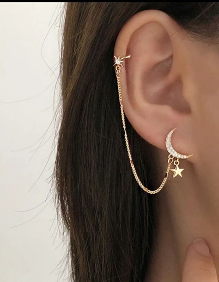 a woman wearing a gold chain ear cuff with stars and moon charms on the end