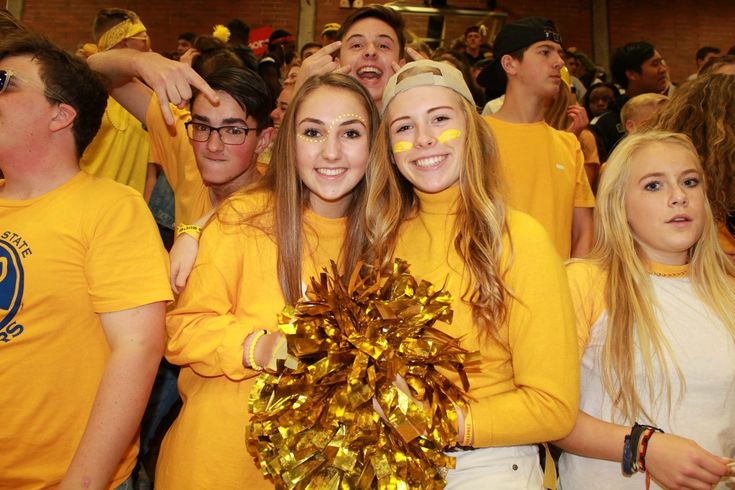 two girls in yellow cheerleader shirts are surrounded by other people