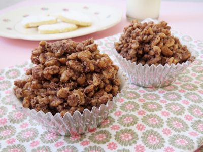 two cups filled with chocolate crumbles on top of a pink table cloth next to a plate of cookies