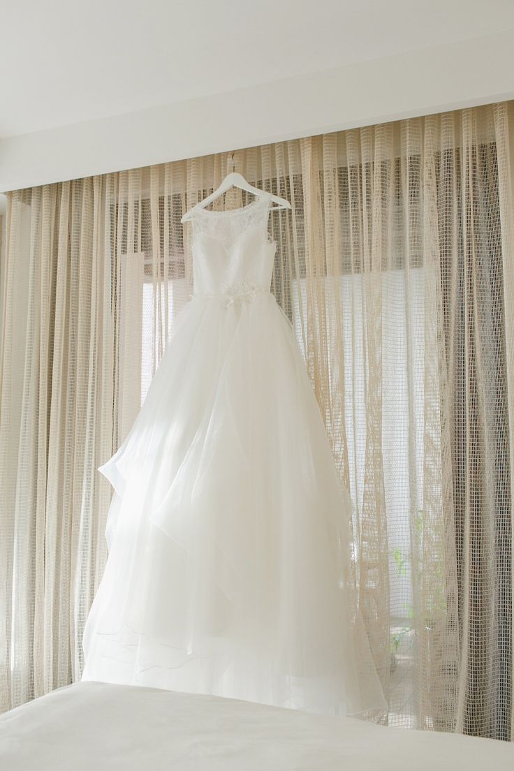 a wedding dress hanging on a hanger in front of a window with sheer drapes