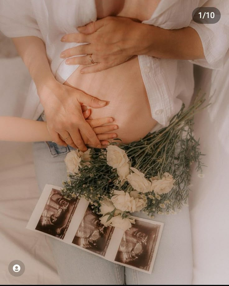 a pregnant woman is holding her stomach with flowers on the table next to it and photos