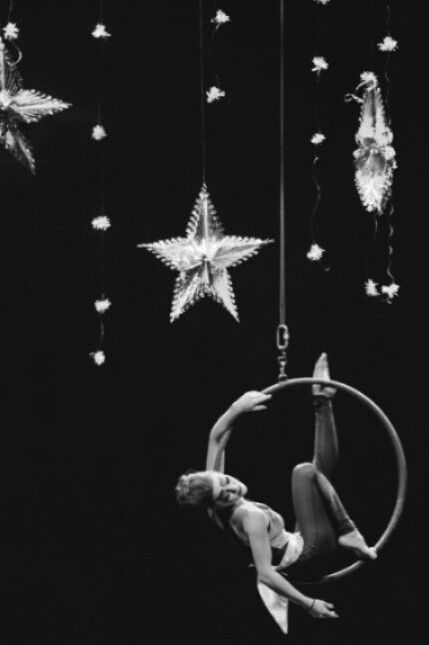 a woman is doing aerial acrobatics in front of hanging stars and lights