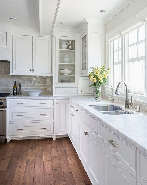 a kitchen with white cabinets and wood floors is pictured in this image, there are flowers on the counter