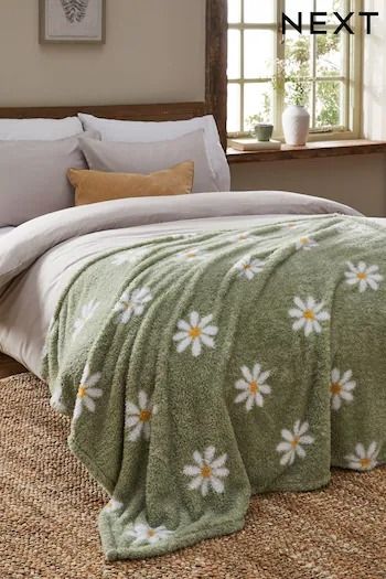 a bed covered in a green blanket with white daisies on it next to a window