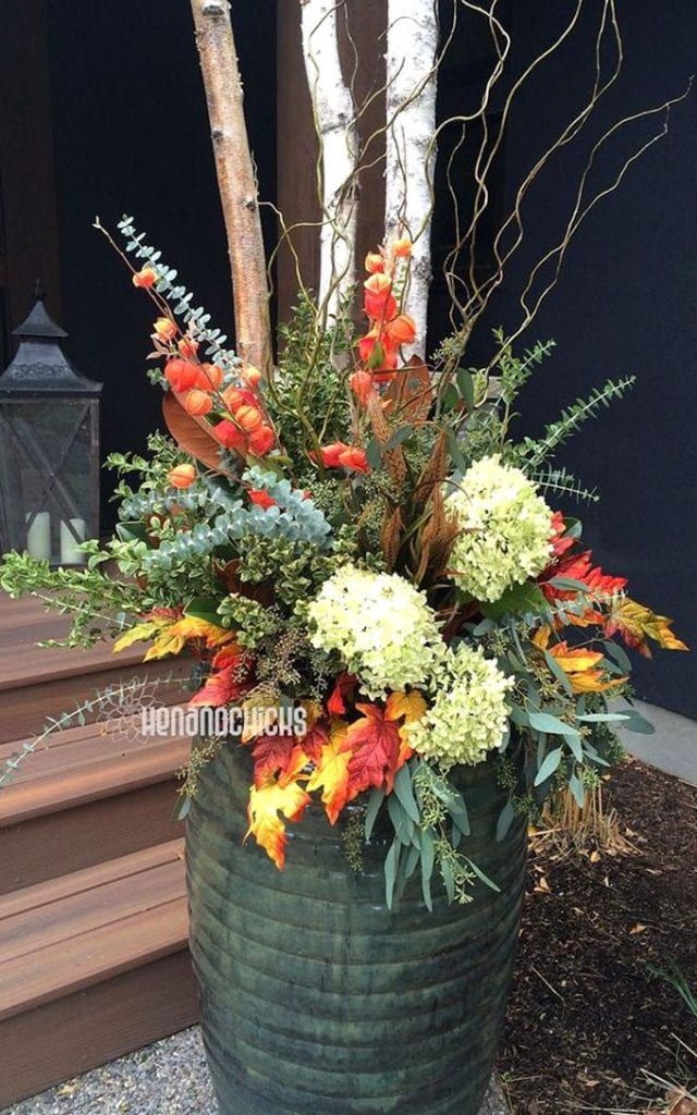 an arrangement of flowers in a green basket on the front steps of a house with stairs leading up to it