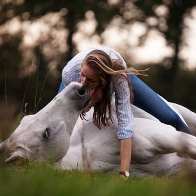 a woman laying on the ground next to a white horse with it's head down