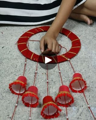 a woman is making red decorations with string and beads on the floor in front of her