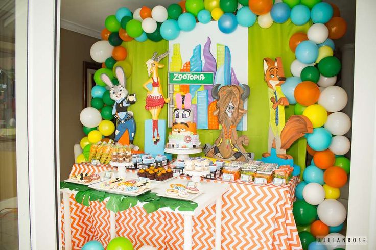 a birthday party with balloons and decorations on the wall, including an animal themed dessert table