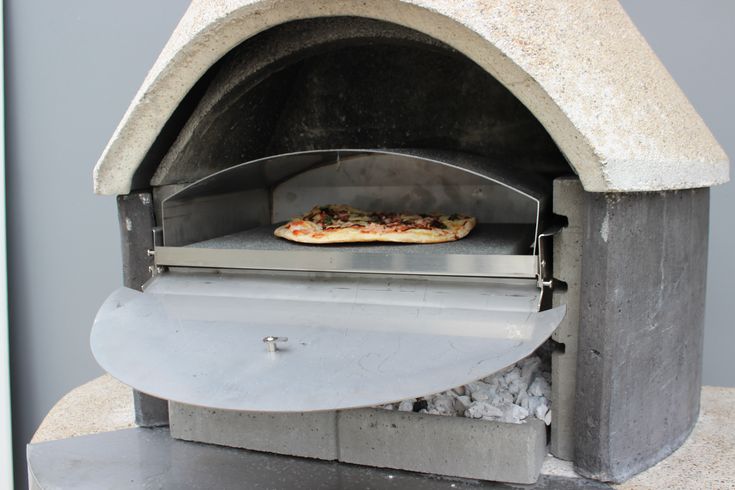 a pizza baking in an outdoor oven with rocks and gravel on the bottom shelf,