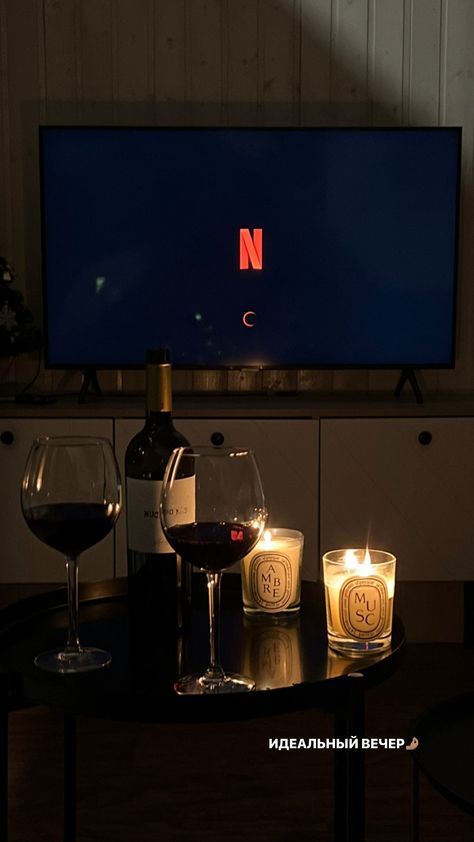 two wine glasses sitting on a table in front of a flat screen tv with candles