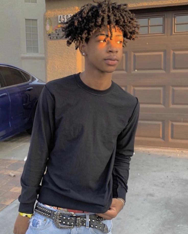 a young man with dreadlocks standing in front of a car and wearing a black shirt