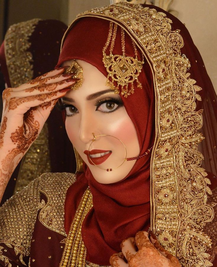 a woman wearing a red and gold bridal outfit holding her hands to her face