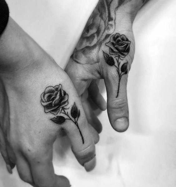 two people holding hands with tattoos on their fingers and one has a rose tattooed on it