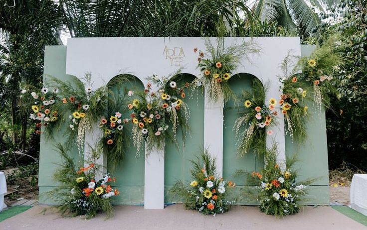 an outdoor ceremony with flowers and greenery hanging from the wall, decorated with arches