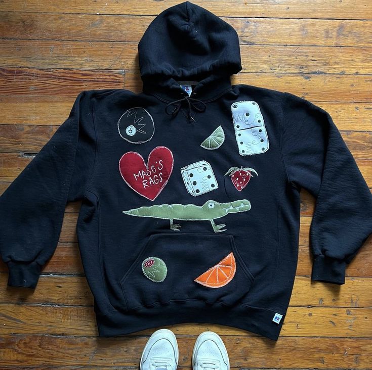 a black hoodie with dices, hearts, and alligator on it next to white shoes