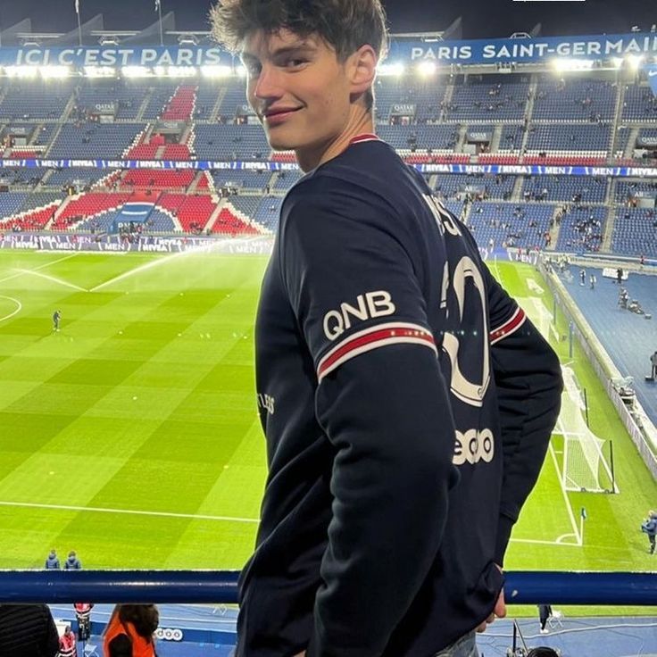 a young man standing in front of a soccer field with the stadium lights behind him