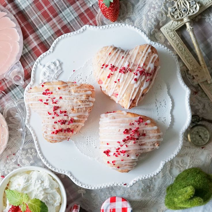 two heart shaped pastries on a plate with strawberries and whipped cream in the background