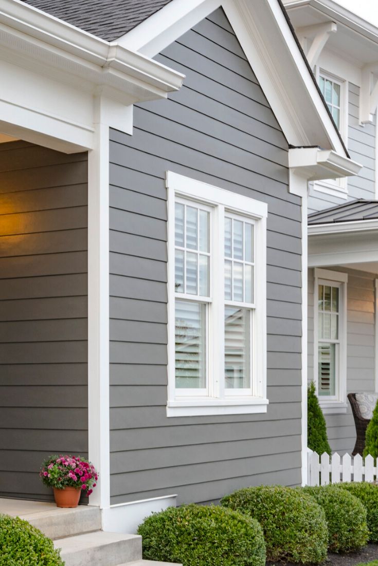 a house with gray siding and white trim, trimmed in boxwood shrubs on the front lawn