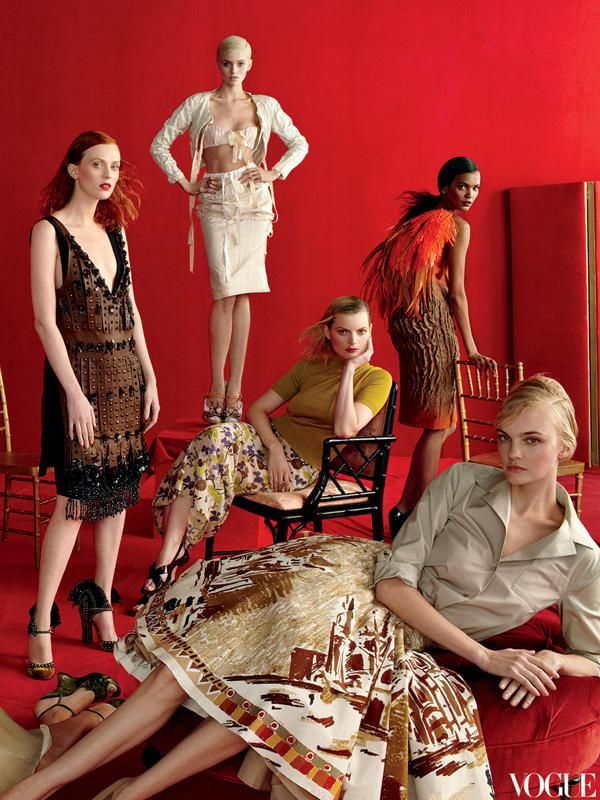 the models are posing in front of red walls and colorful furniture, with one woman sitting on a chair