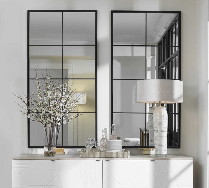 a white dresser topped with two mirrors next to a lamp and vase filled with flowers