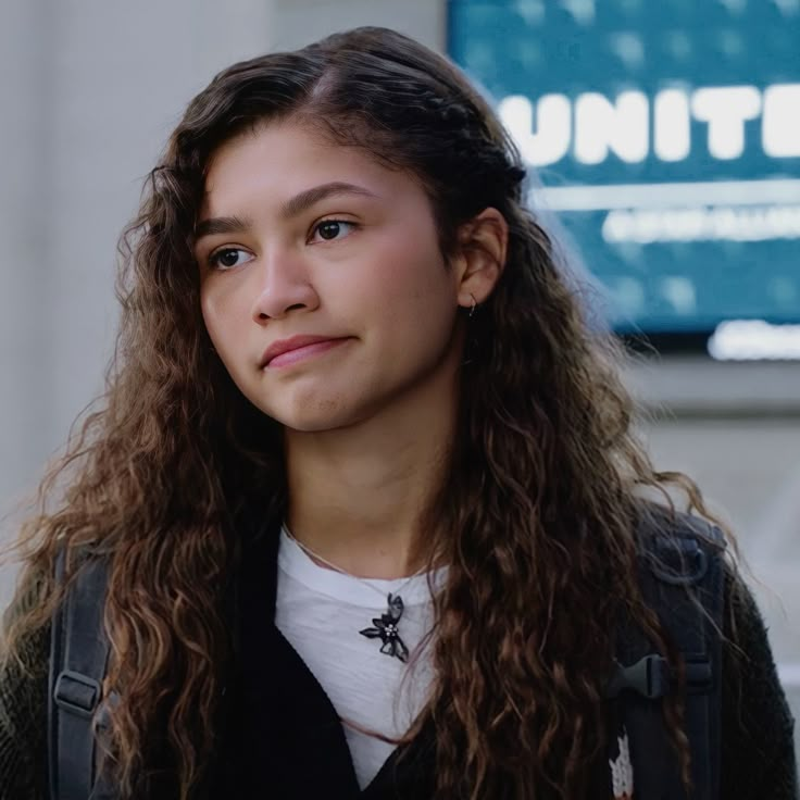 a woman with long curly hair standing in front of a white wall and looking at the camera