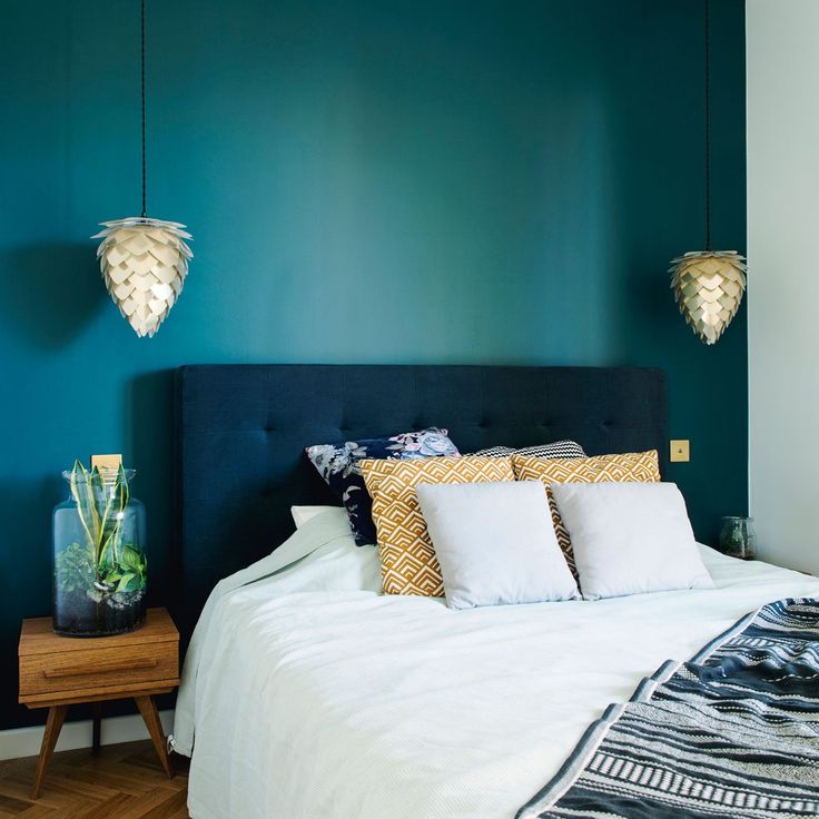 a bedroom with green walls and white bedding, two hanging lights above the bed