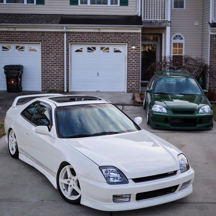 two white cars parked in front of a brick building with garage doors on each side