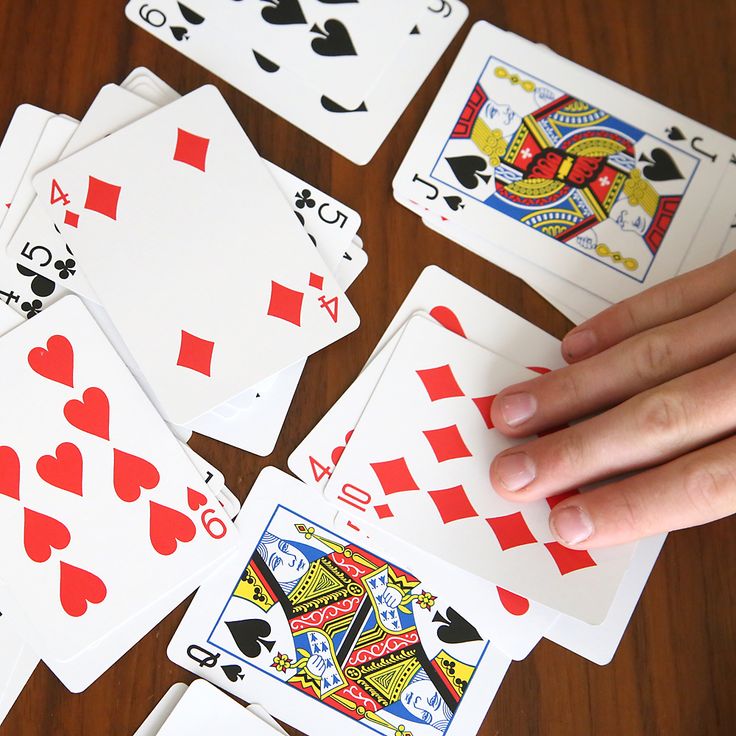 four hands holding playing cards on top of a wooden table next to other playing cards