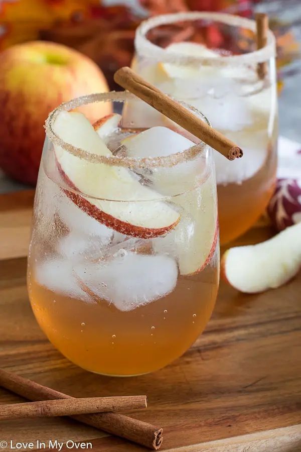 two glasses filled with apple cider on top of a cutting board