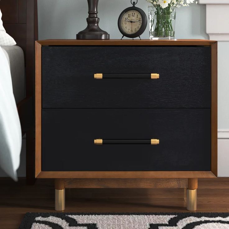 a nightstand with two drawers and a clock next to it on a rug in front of a bed