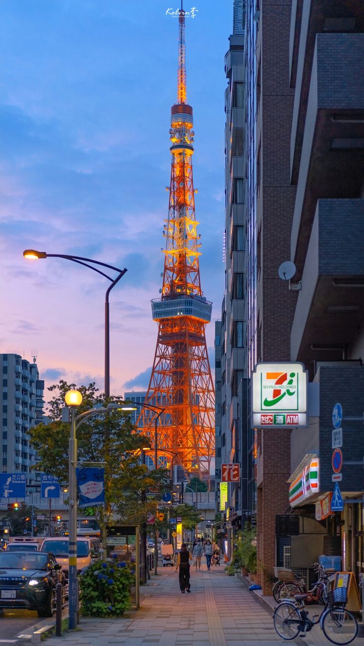 the eiffel tower is lit up at night, with people walking down the sidewalk