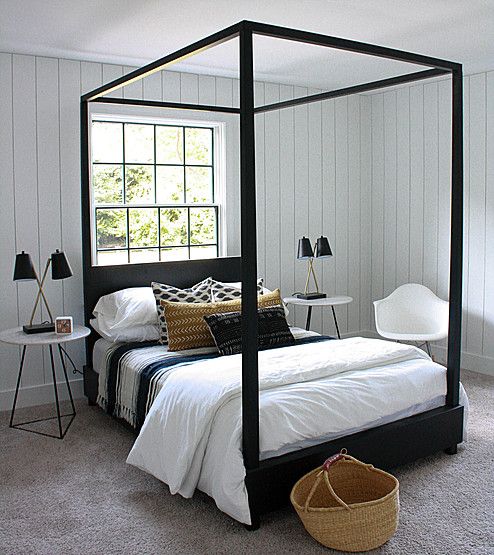 a bedroom with white walls and carpeted flooring has a four poster bed in the corner