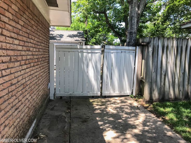 a white fence next to a brick building and tree in the back yard with green grass